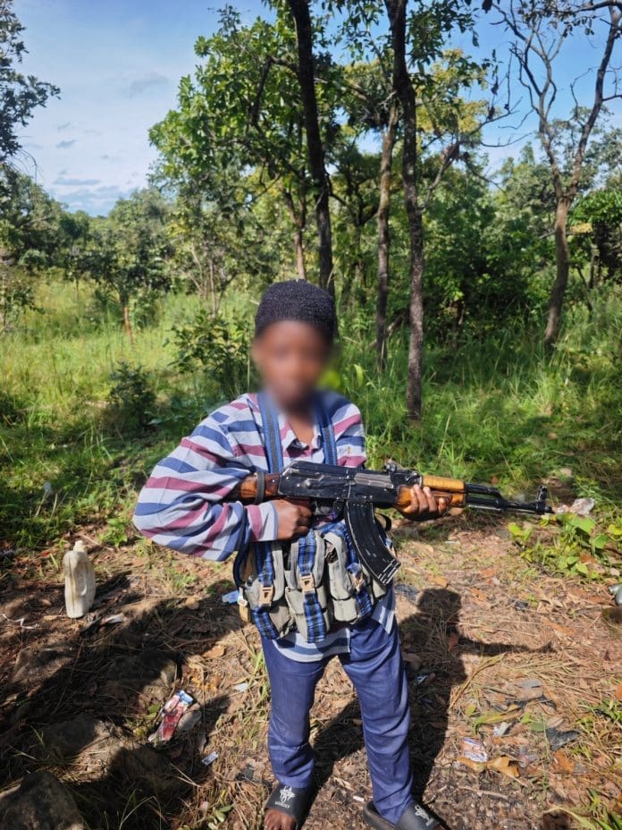 An 11-year-old boy poses with an AK 47 assault gun at an location in the bush after their abduction in September. Family claims the children were trained to become child-kidnappers. (Credit: distress family member).